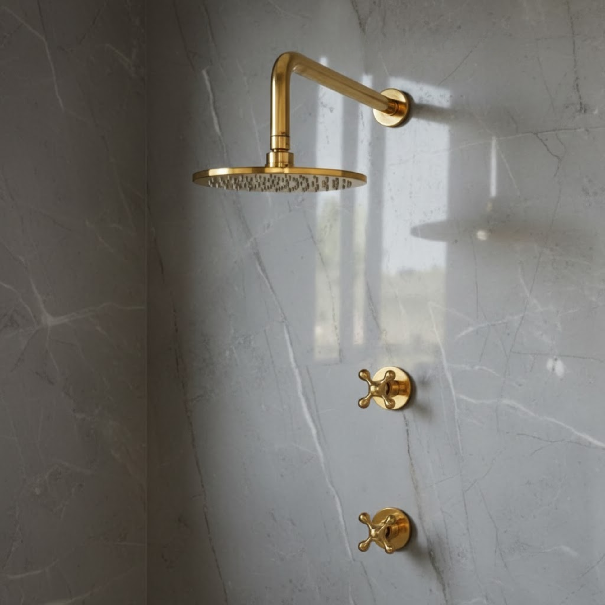 Profile view of an unlacquered brass rainfall shower head and two vintage-style cross control handles installed on light gray marble tile.