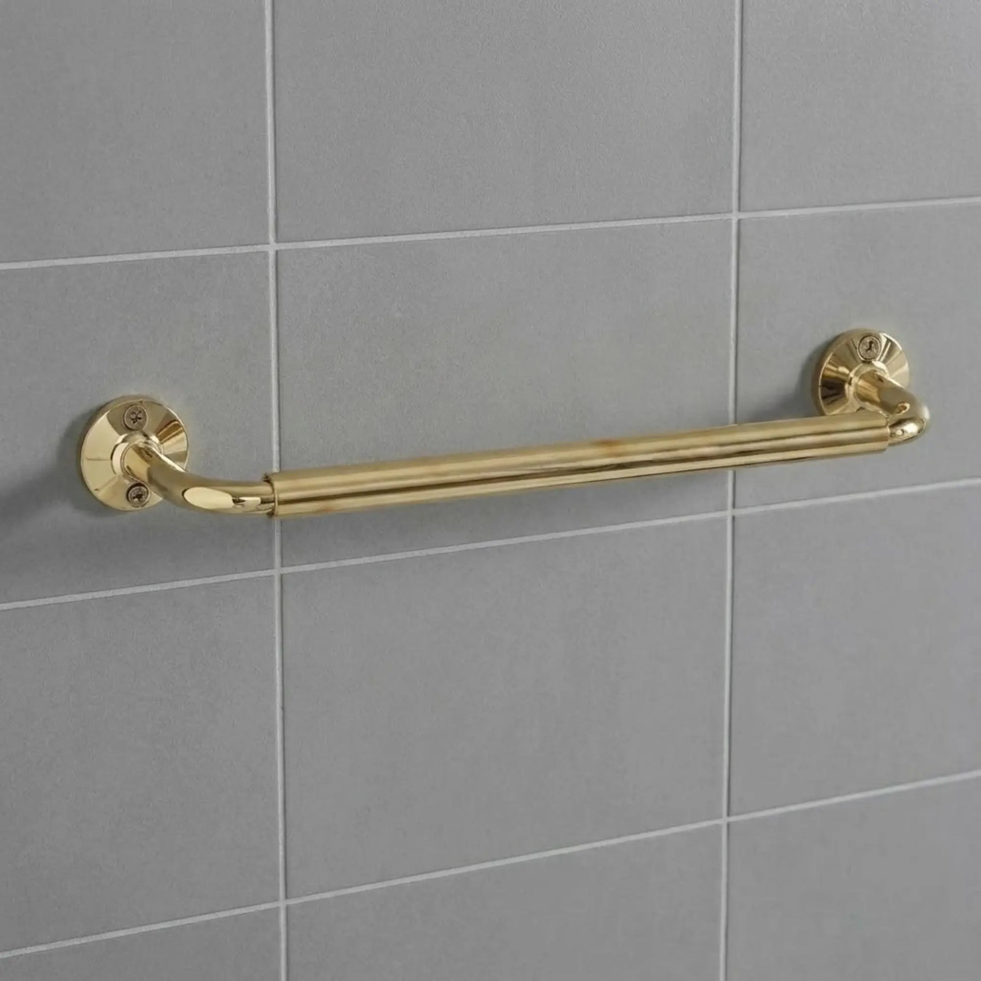 Unlacquered brass wall-mounted grab bar installed on grey subway tiles, featuring traditional round decorative flanges and exposed screws.