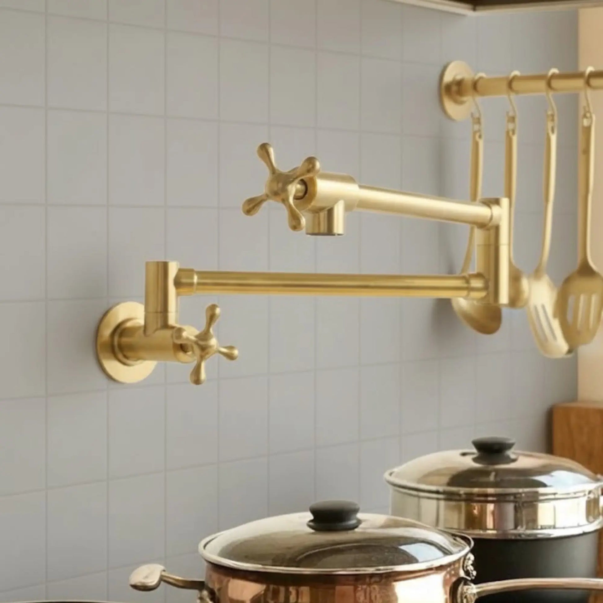 Gold kitchen faucet mounted on a tiled wall with pots below.