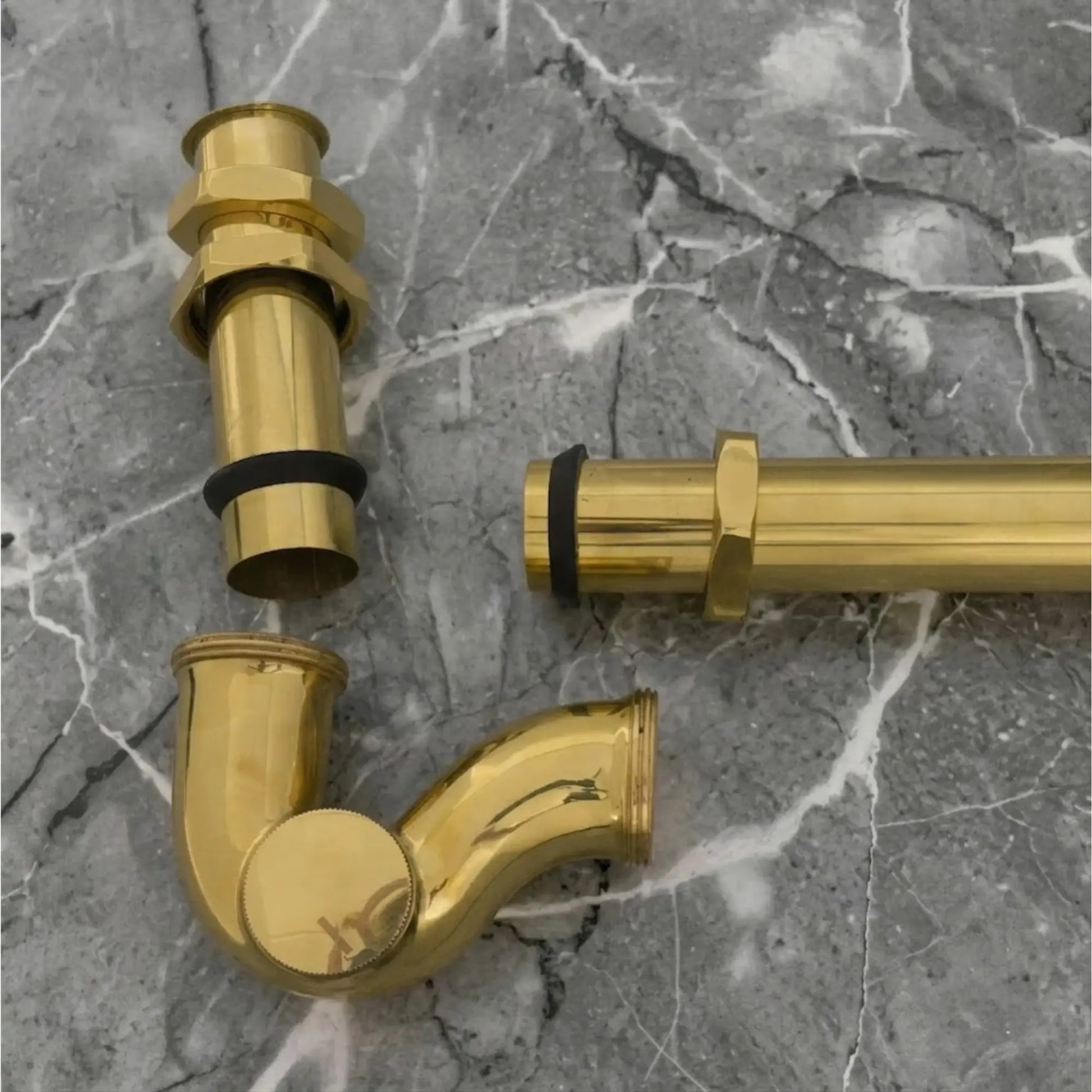 Solid unlacquered brass bathroom sink P-trap drain kit with exposed brass plumbing parts on gray marble surface