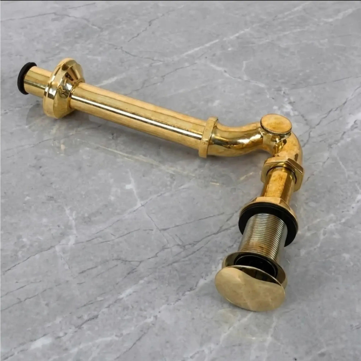 Solid unlacquered brass bathroom sink P-trap drain pipe kit with exposed luxury brass plumbing on gray marble surface