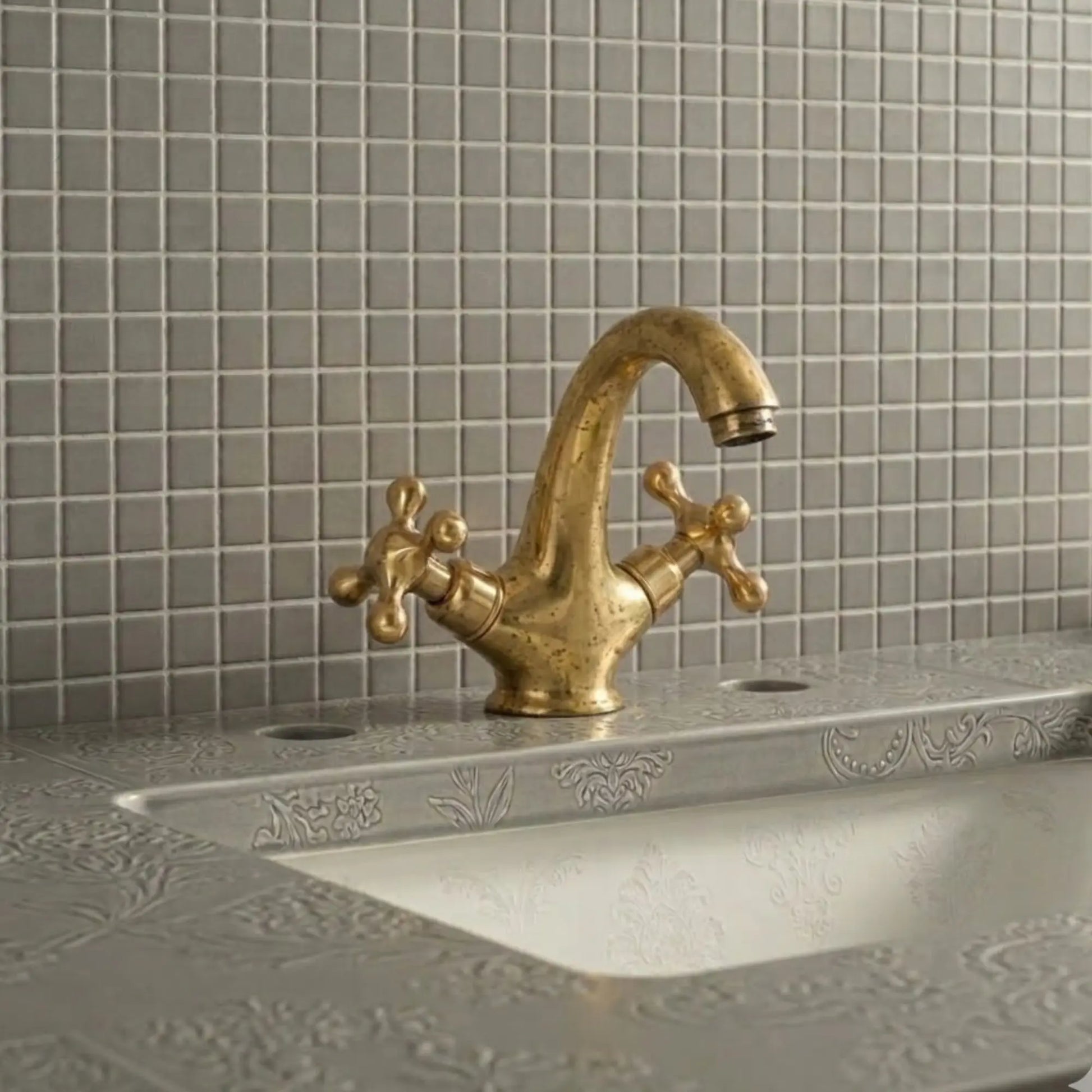 Unlacquered brass bathroom sink faucet with cross handles showing natural living patina on decorative vanity sink