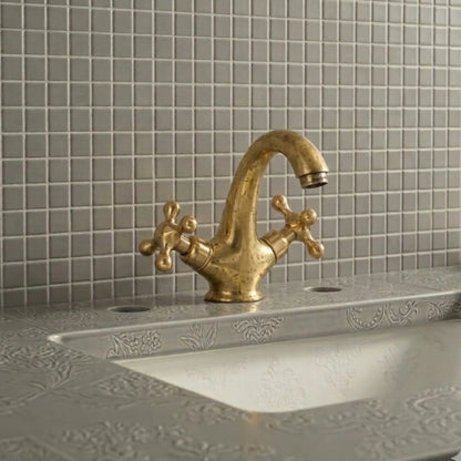 Unlacquered brass bathroom sink faucet with cross handles showing natural living patina on decorative vanity sink