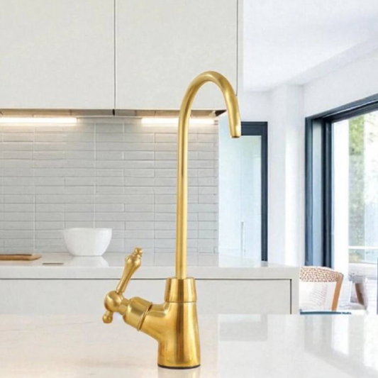 Handcrafted unlacquered brass beverage faucet installed on a white marble kitchen island.