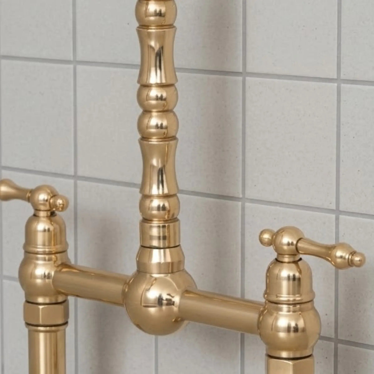 Close-up detail of unlacquered brass bridge kitchen faucet with lever handles and solid brass construction