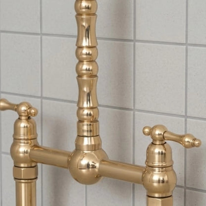 Close-up detail of unlacquered brass bridge kitchen faucet with lever handles and solid brass construction