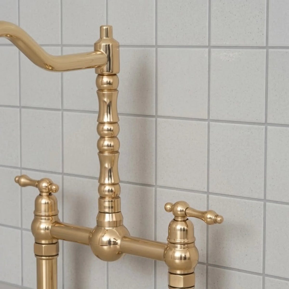 Unlacquered brass bridge kitchen faucet with cross handles and high arc spout installed against tiled backsplash
