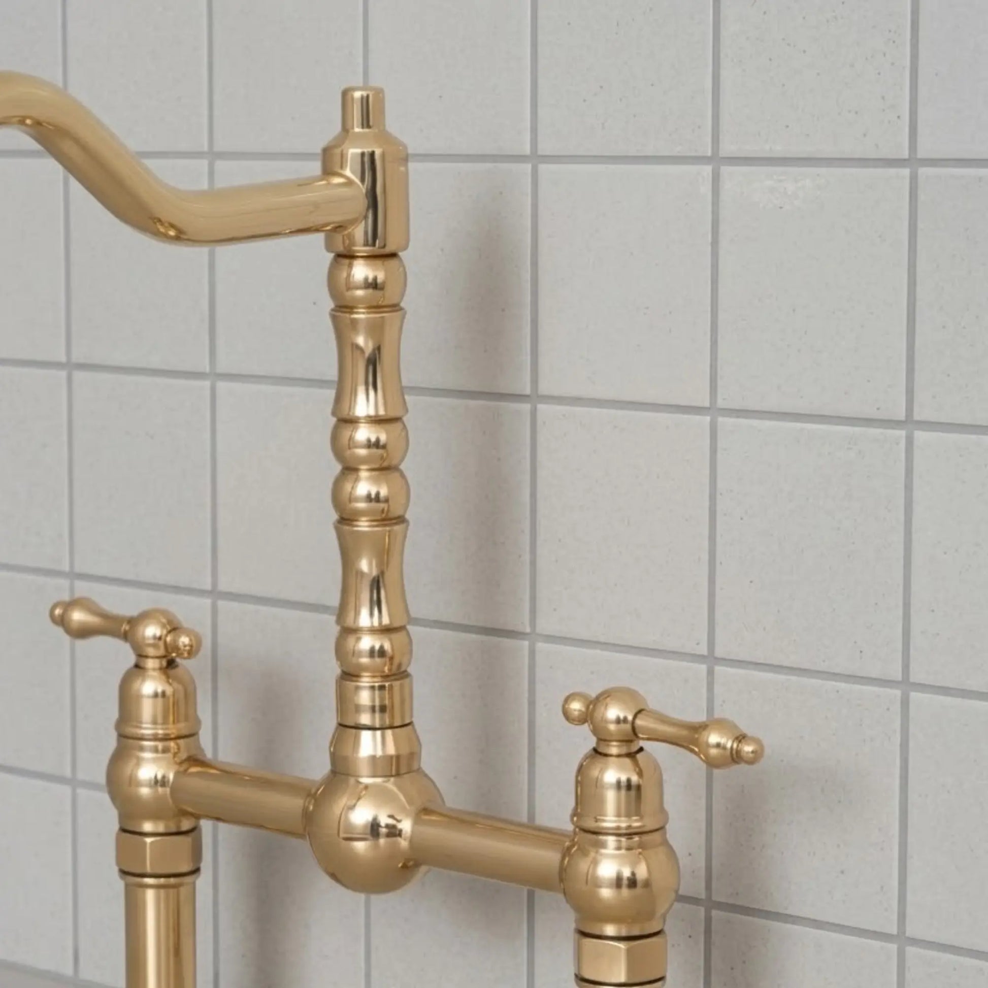 Unlacquered brass bridge kitchen faucet with cross handles and high arc spout installed against tiled backsplash