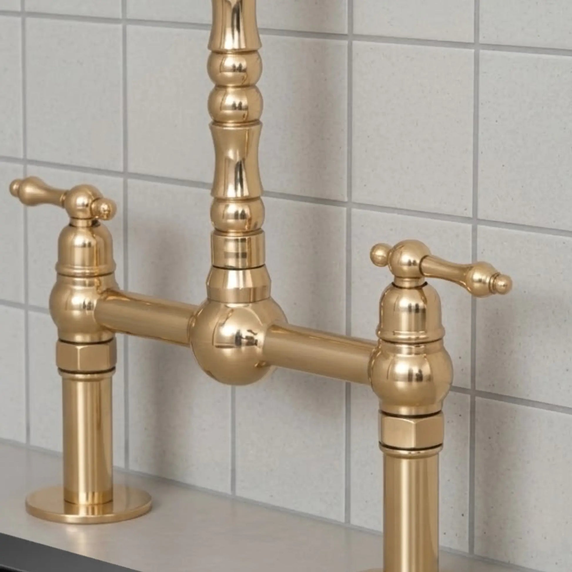 Unlacquered brass bridge kitchen faucet with cross handles installed on countertop with tiled backsplash