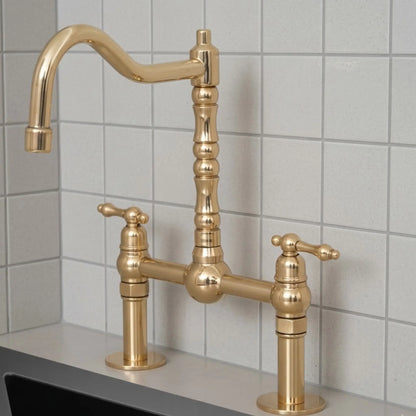 Unlacquered brass bridge kitchen faucet with lever handles and high arc spout installed on countertop with tiled backsplash