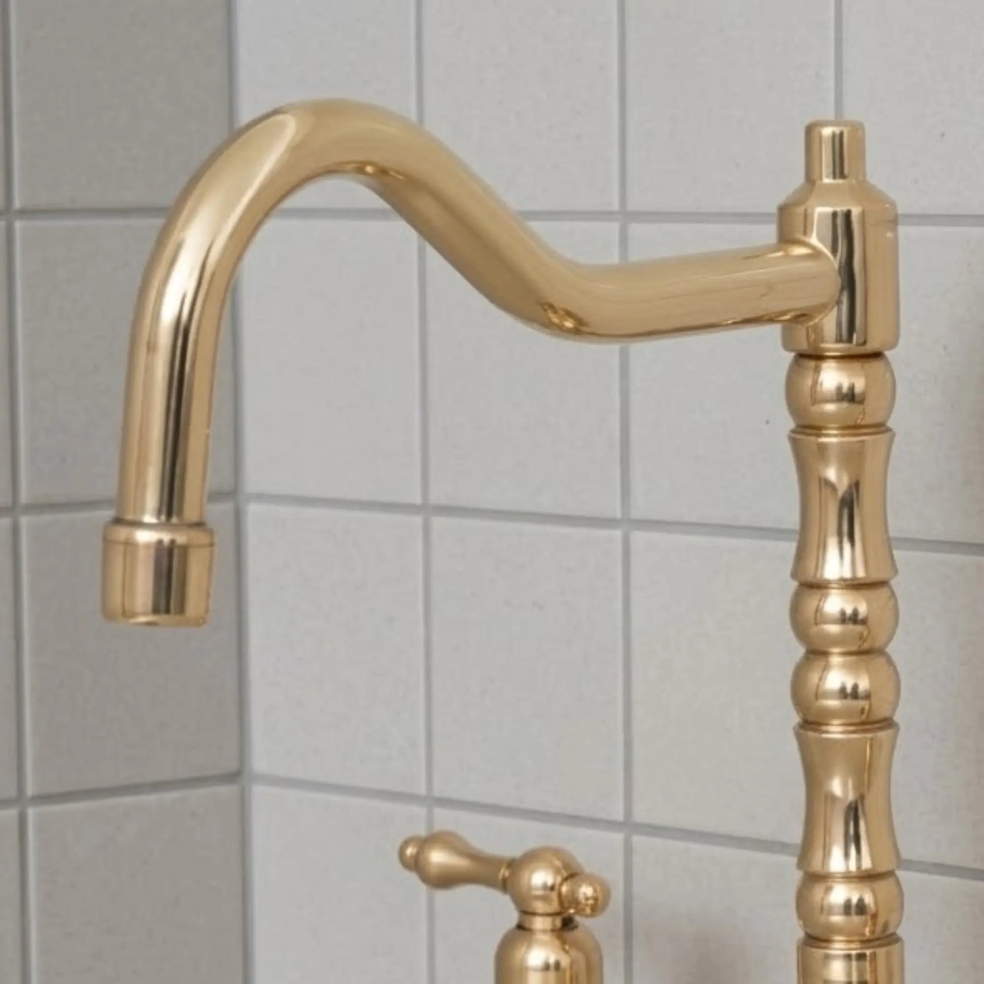 Unlacquered brass bridge kitchen faucet with high arc spout and vintage design installed on countertop with tiled backsplash