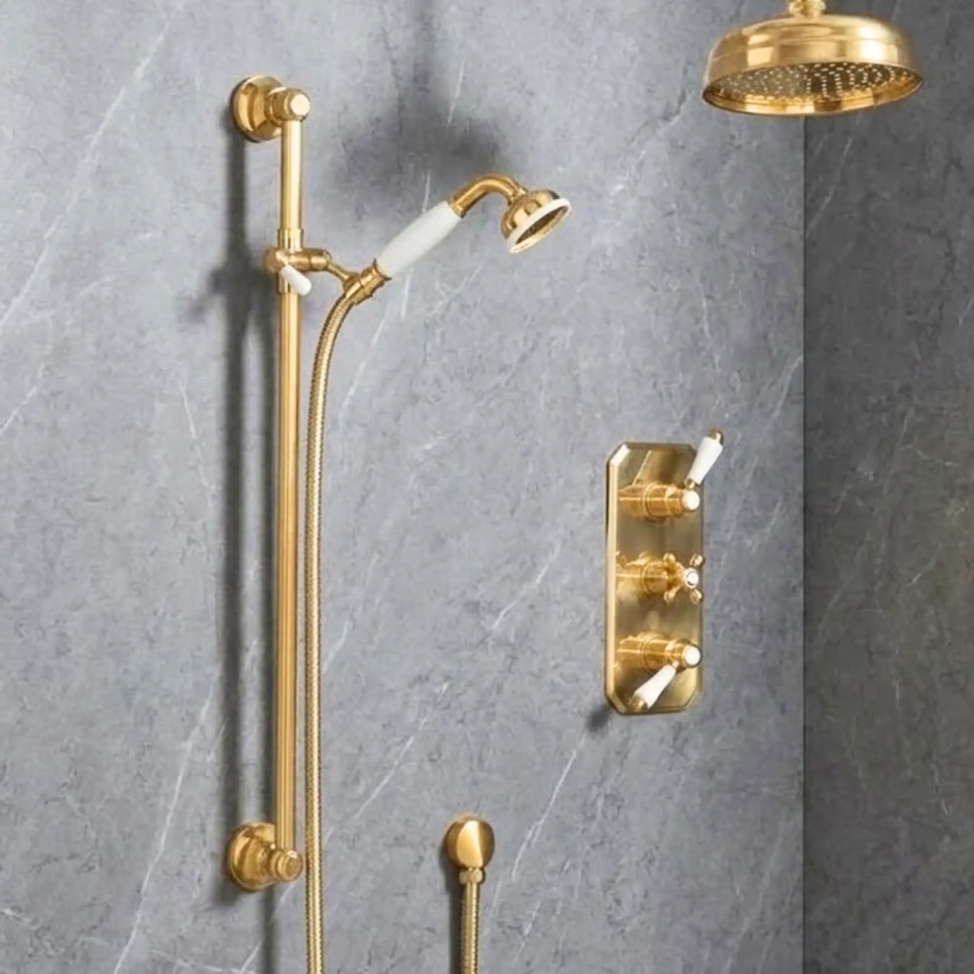 Full view of unlacquered brass concealed thermostatic shower system with rainfall head, slide rail, porcelain handshower, and trim plate on grey marble wall