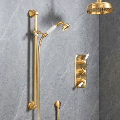 Full view of unlacquered brass concealed thermostatic shower system with rainfall head, slide rail, porcelain handshower, and trim plate on grey marble wall