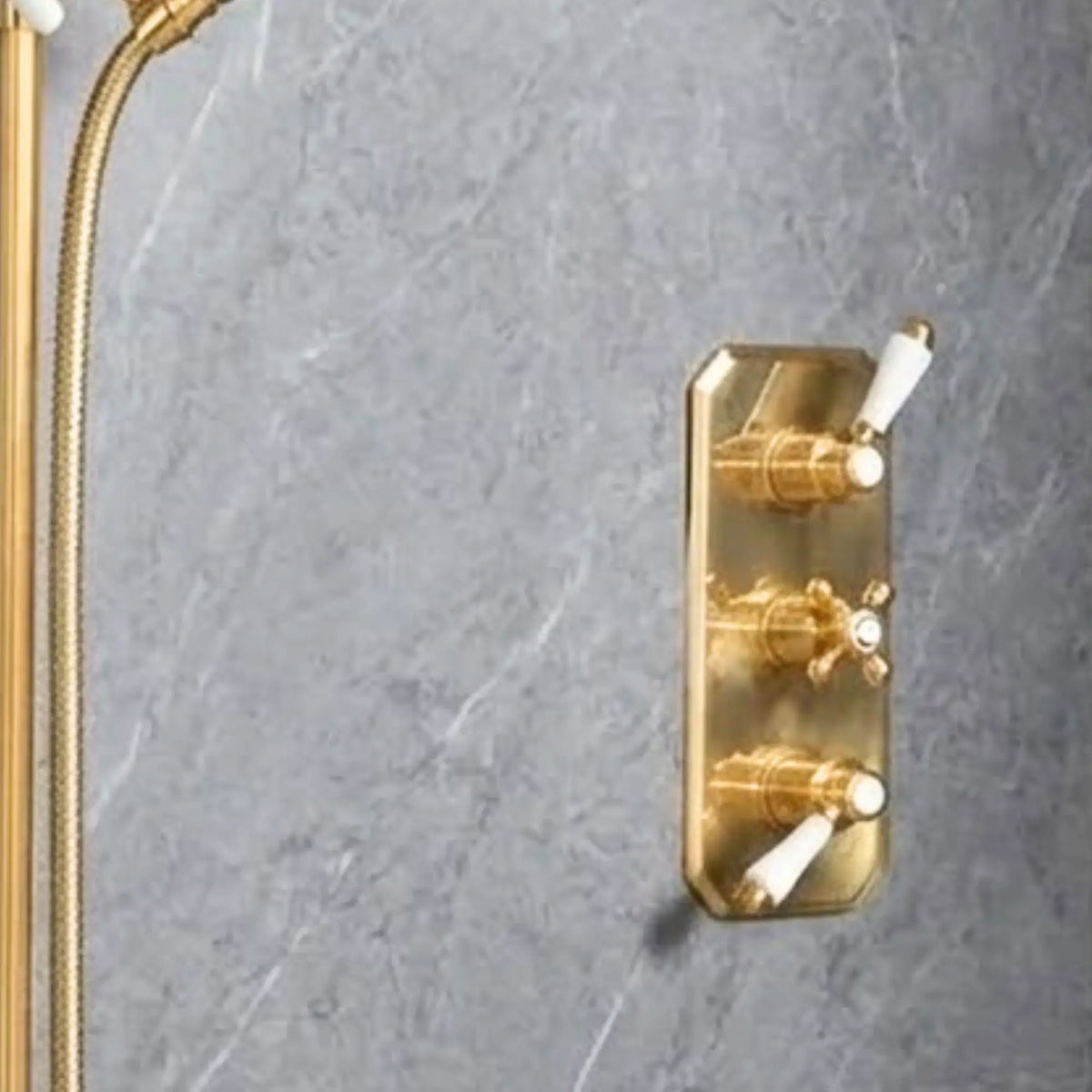 Close-up of unlacquered brass concealed thermostatic shower system showing adjustable slide rail, braided hose, porcelain-handle handshower, and rainfall head on grey marble wall