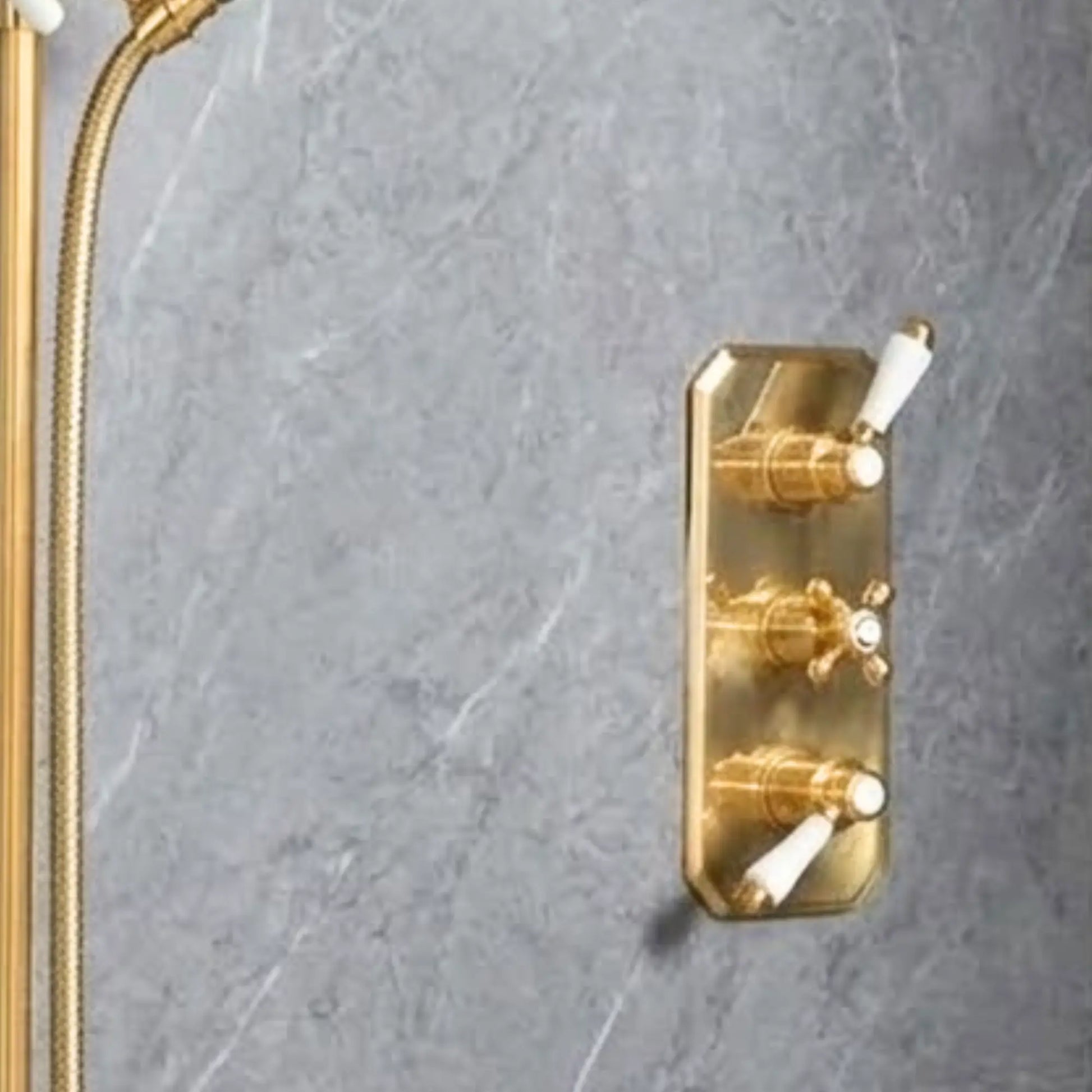Close-up of unlacquered brass concealed thermostatic shower system showing adjustable slide rail, braided hose, porcelain-handle handshower, and rainfall head on grey marble wall