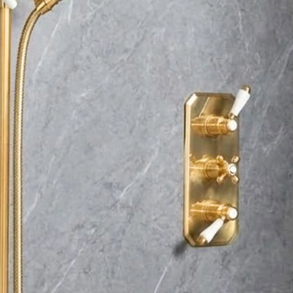 Close-up of unlacquered brass concealed thermostatic shower system showing adjustable slide rail, braided hose, porcelain-handle handshower, and rainfall head on grey marble wall