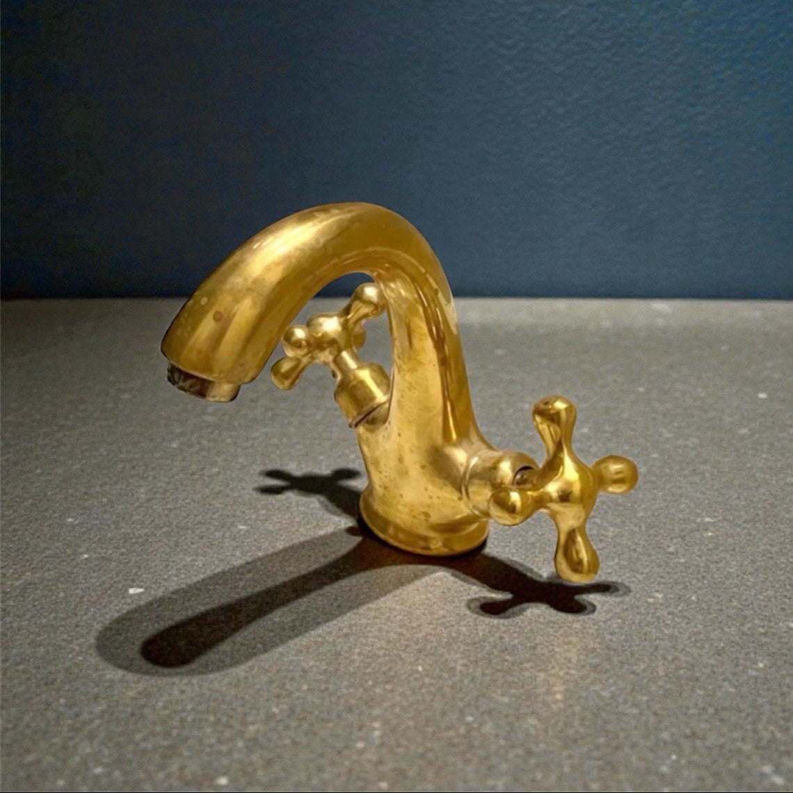 Unlacquered brass bathroom faucet featuring traditional double cross handles and living finish