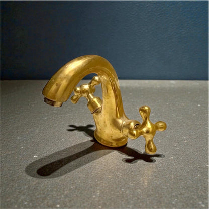 Unlacquered brass bathroom faucet featuring traditional double cross handles and living finish