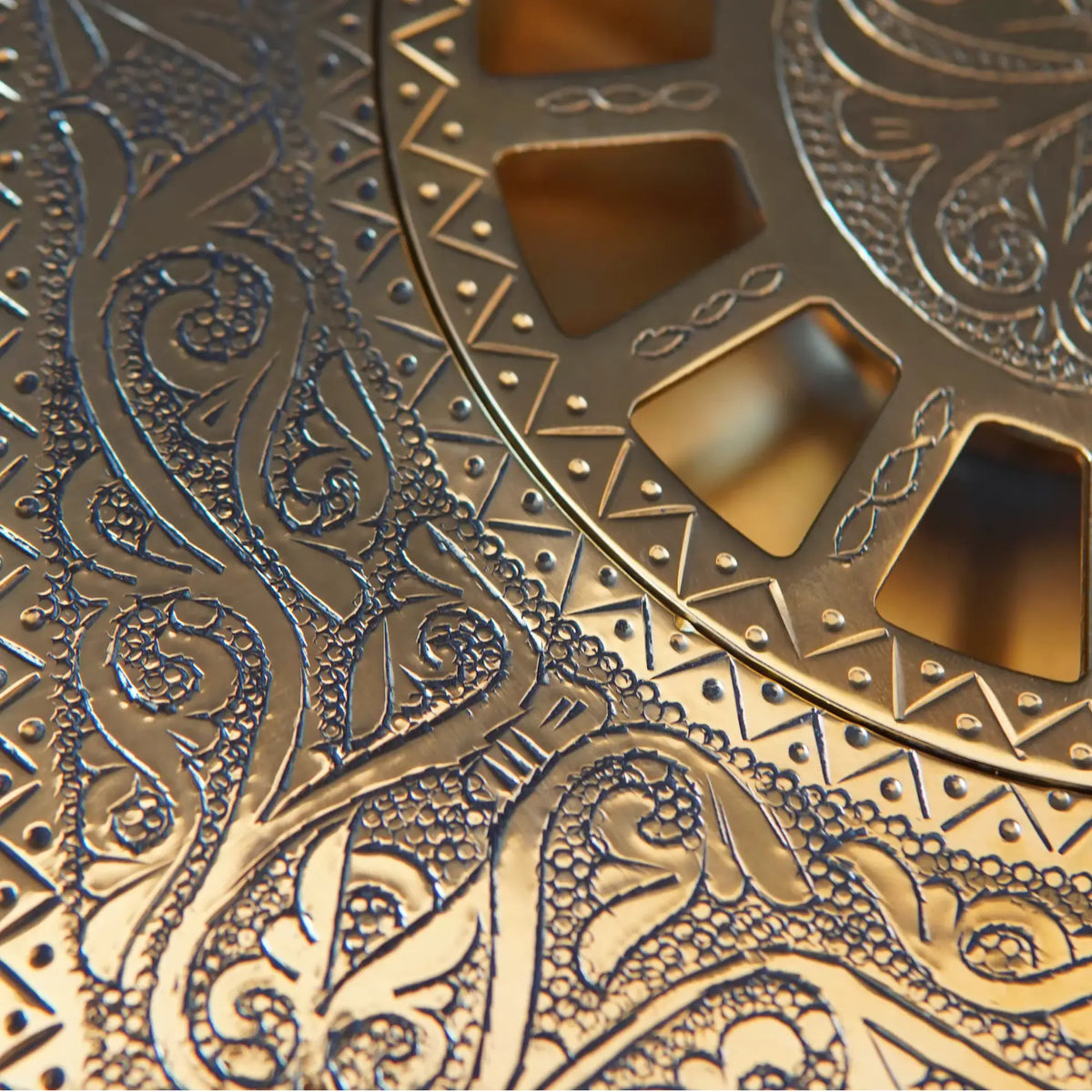 Macro close-up of hand-engraved scrollwork and dot pattern on solid unlacquered brass shower floor drain