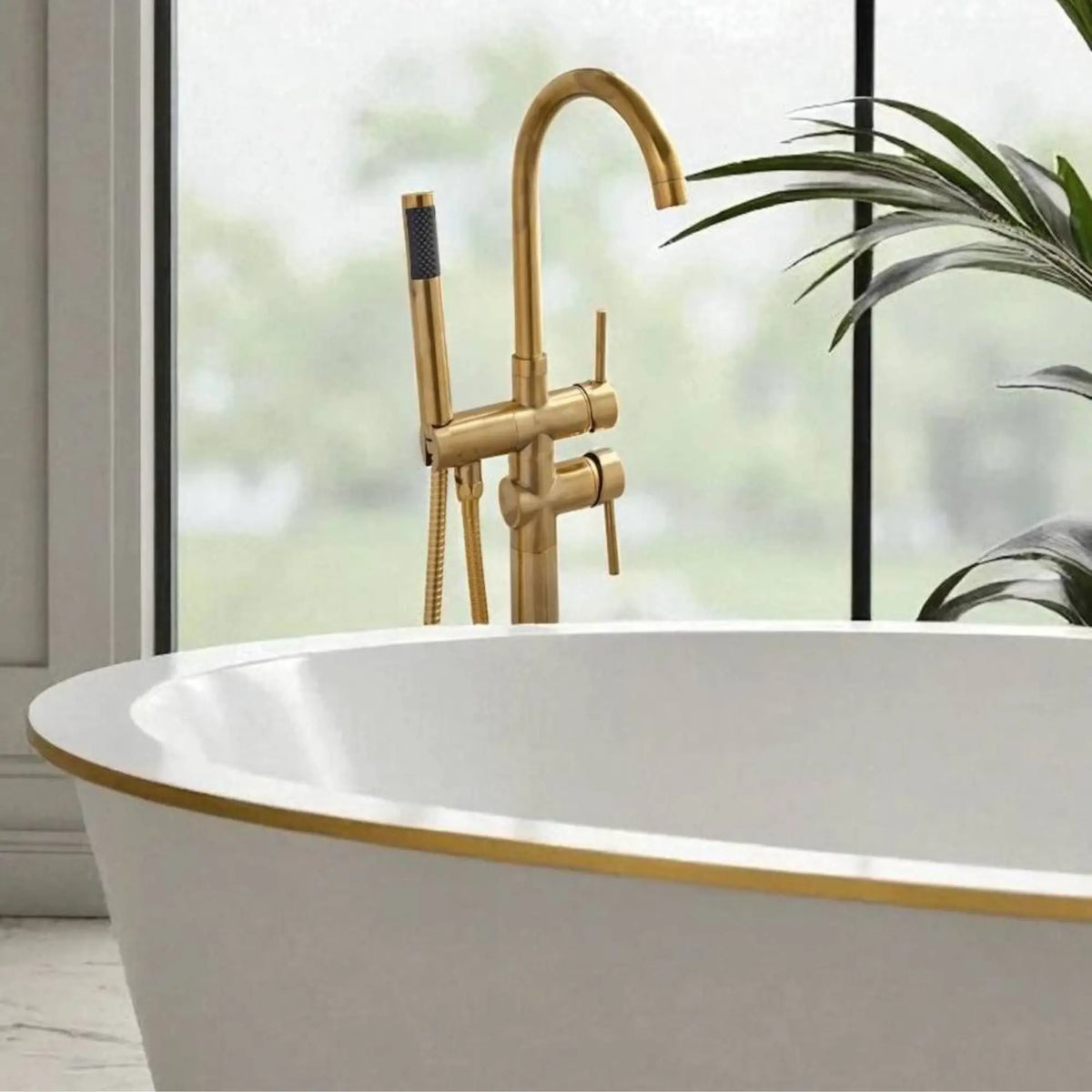 Close-up of the unlacquered brass floor-mount bathtub faucet showing the dual-handle controls and high-flow handheld shower.