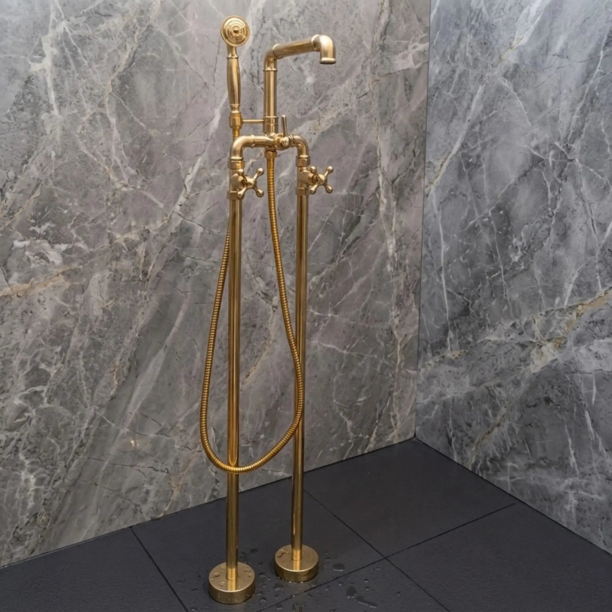 Unlacquered brass freestanding bathtub faucet with handheld shower, solid brass floor mounted tub filler beside gray marble wall