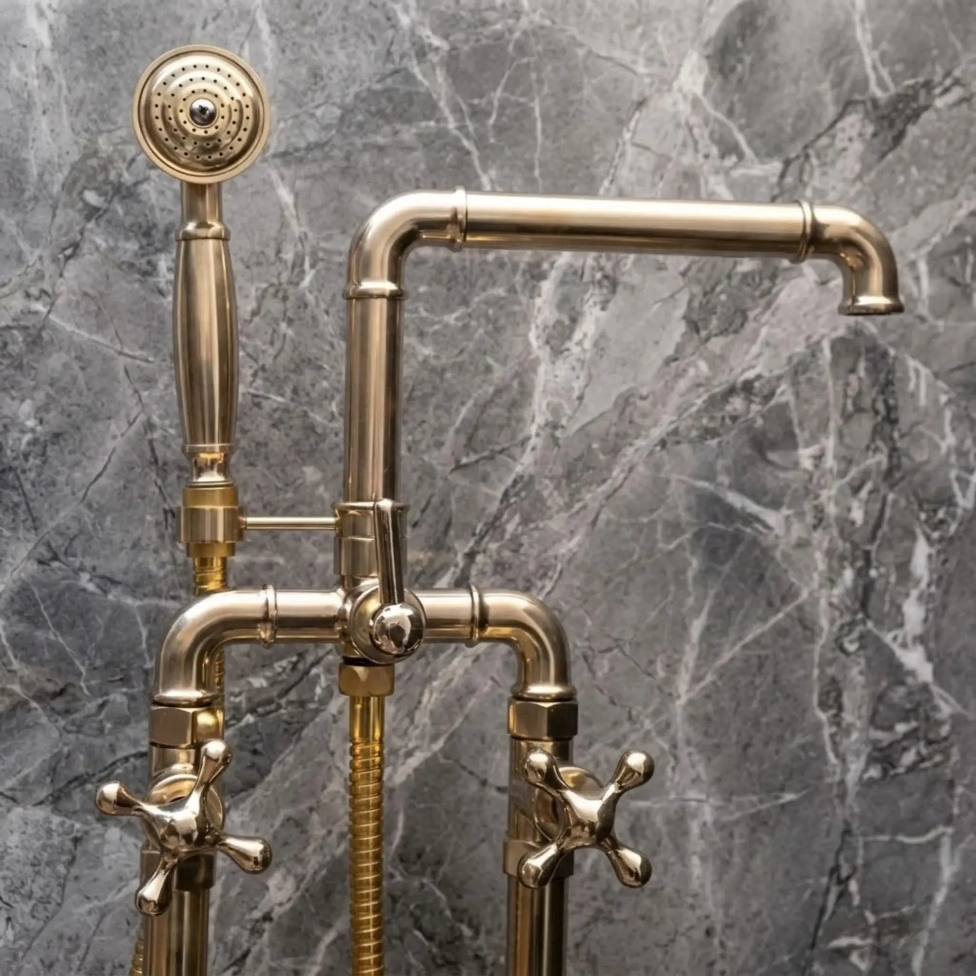 Unlacquered brass freestanding bathtub faucet with handheld shower and cross handles on gray marble wall
