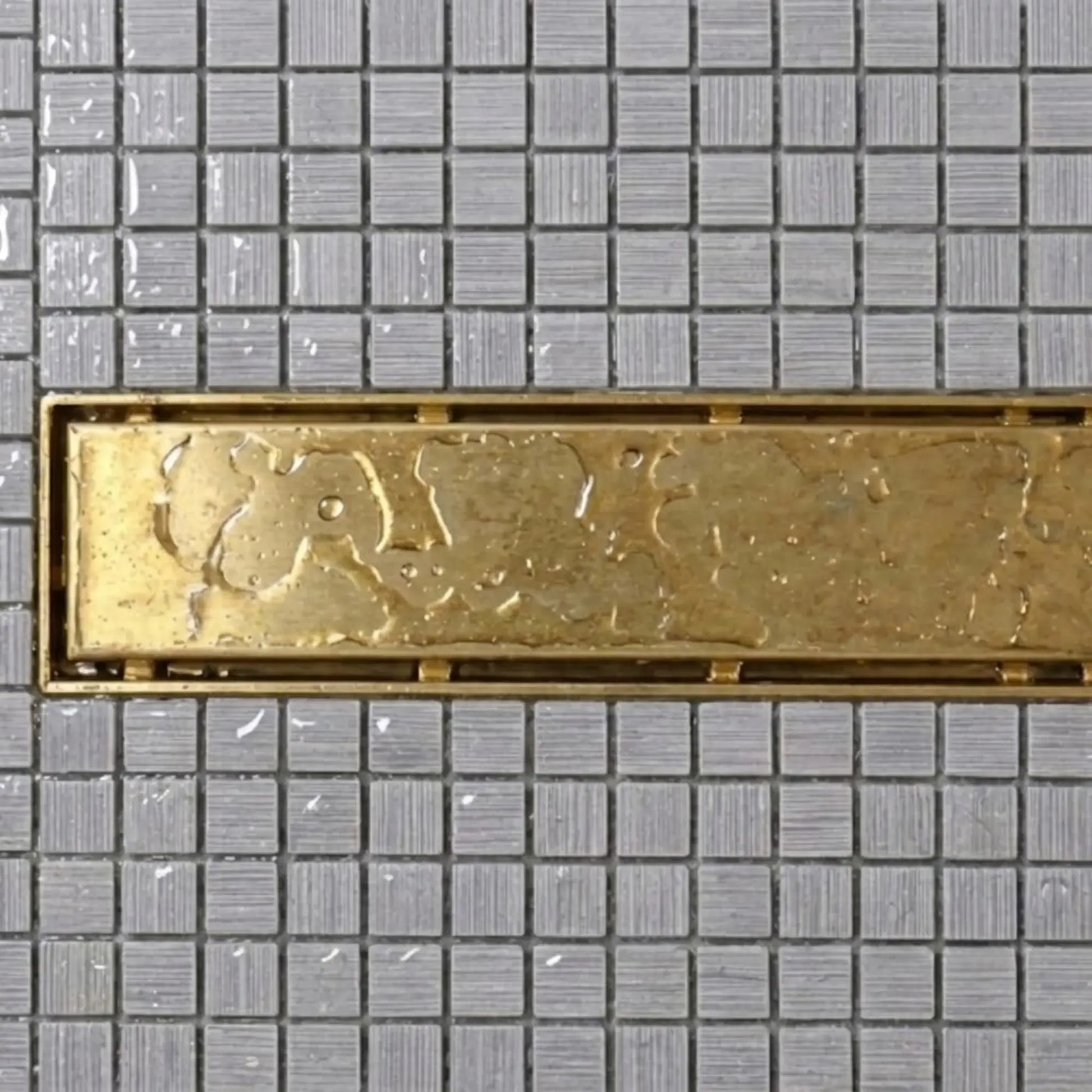 Unlacquered brass linear shower drain overhead view showing natural patina and water-resistant surface on mosaic tile – BrassOna