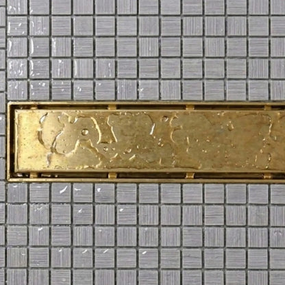 Unlacquered brass linear shower drain top view with water beading on aged patina surface installed in mosaic tile shower – BrassOna