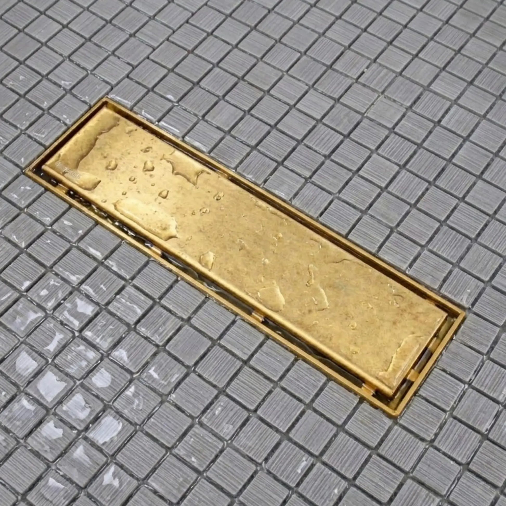 Unlacquered brass linear shower drain with water droplets on mosaic tile – high-flow drainage in action – BrassOna