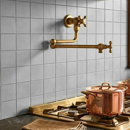 Unlacquered brass wall mount pot filler faucet installed on kitchen backsplash with copper cookware near stove