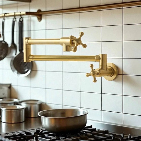 Unlacquered brass wall-mount pot filler with dual cross handles extended over a stainless steel stove in a kitchen with white tile