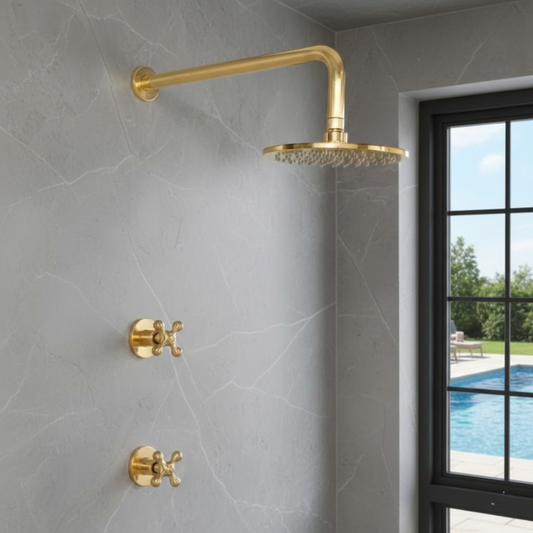Unlacquered brass wall-mounted shower set with 8-inch rainfall shower head and cross handles on a gray marble tiled wall.