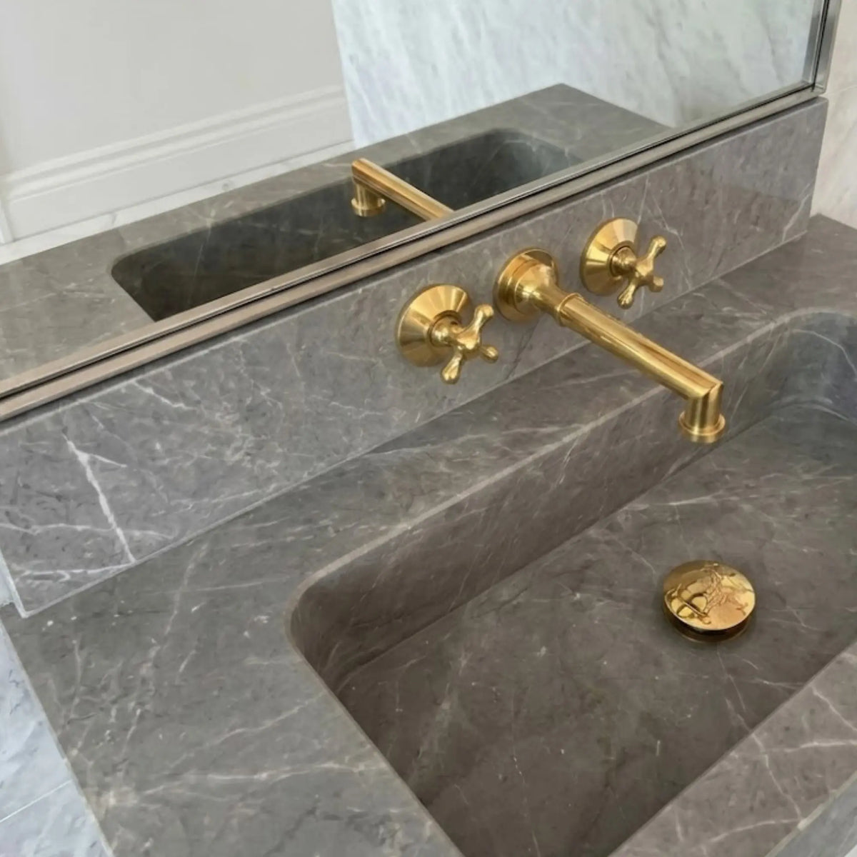 Unlacquered brass wall mount bathroom faucet with 8 inch widespread handles installed on grey marble sink