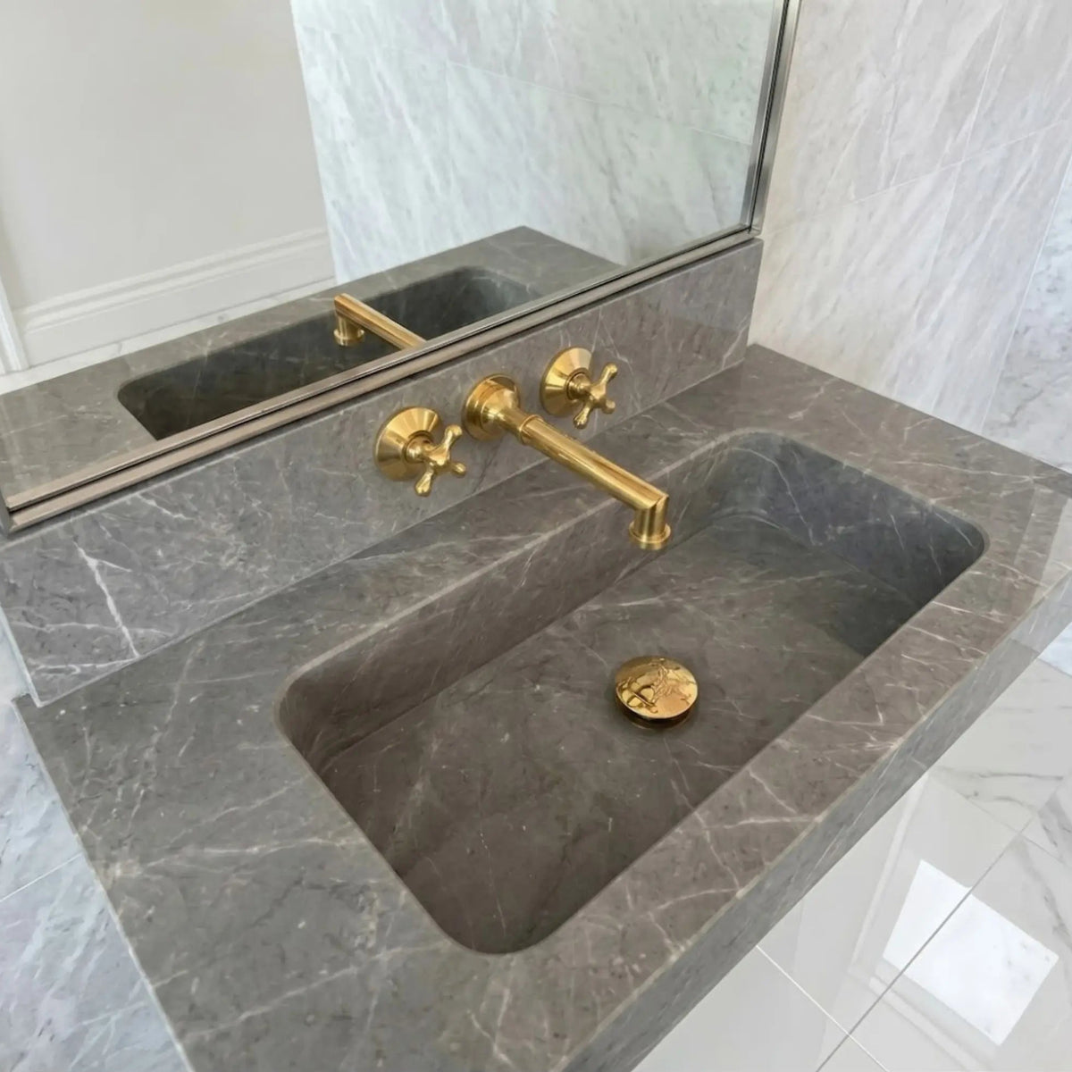 Unlacquered brass wall mount bathroom faucet with 8 inch widespread handles installed on grey marble vanity sink