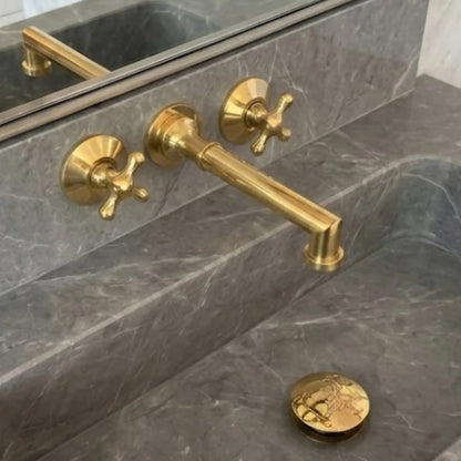 Unlacquered brass wall mount bathroom faucet with 8 inch spout and cross handles installed on marble sink