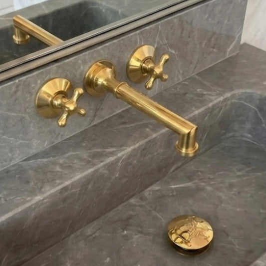 Unlacquered brass wall mount bathroom faucet with 8 inch spout and cross handles installed on marble sink