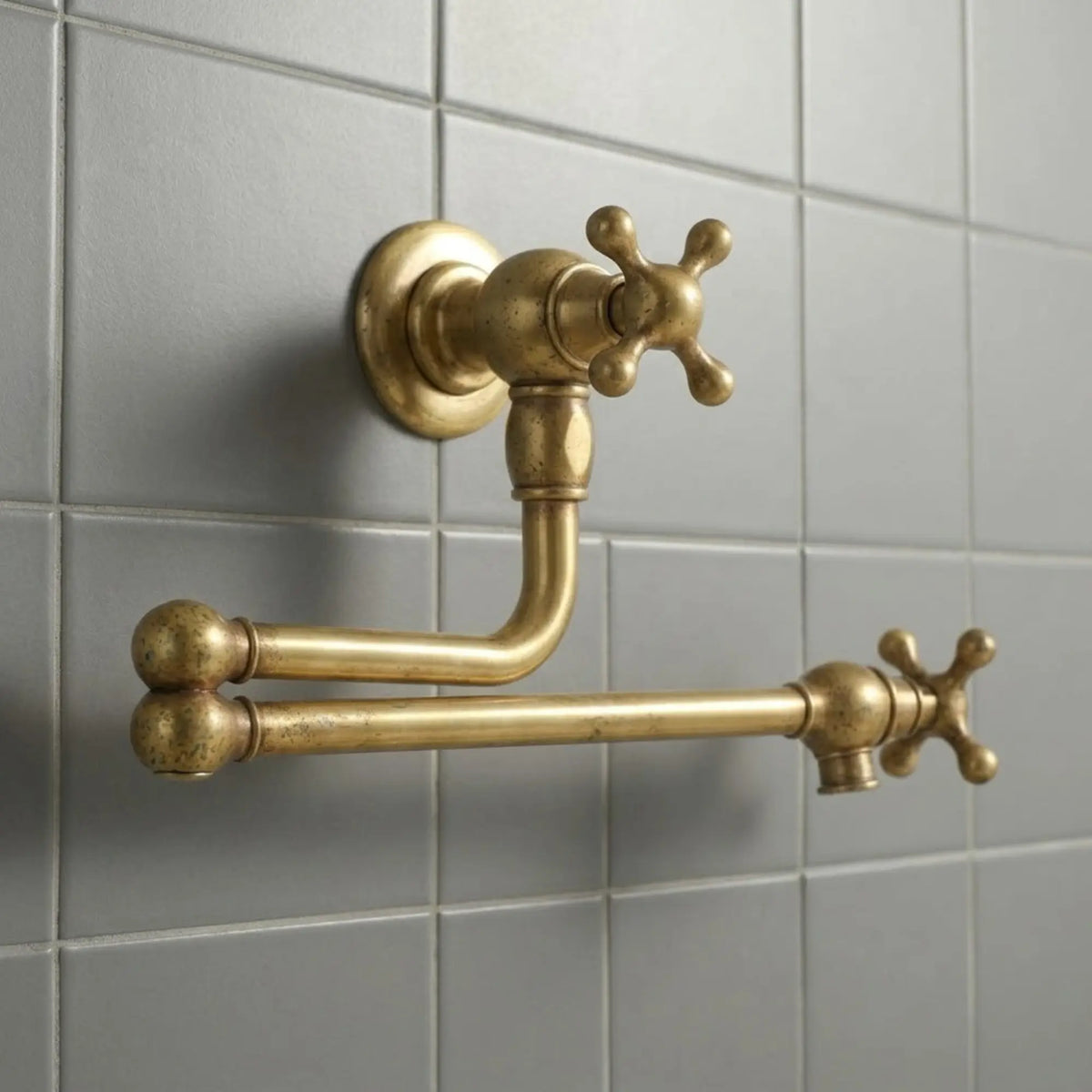 Unlacquered brass wall mount pot filler faucet with retractable arm installed on tiled kitchen wall