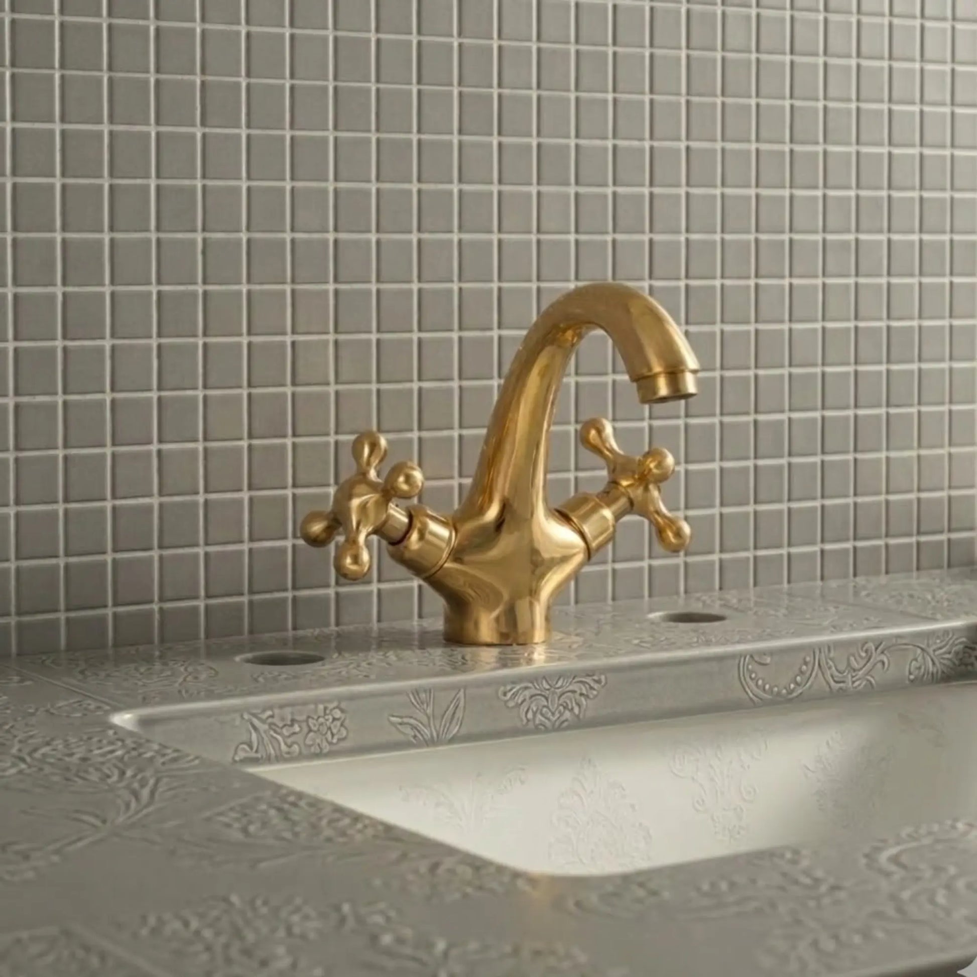 Unlacquered solid brass bathroom sink faucet with cross handles installed on decorative vanity sink with tiled backsplash