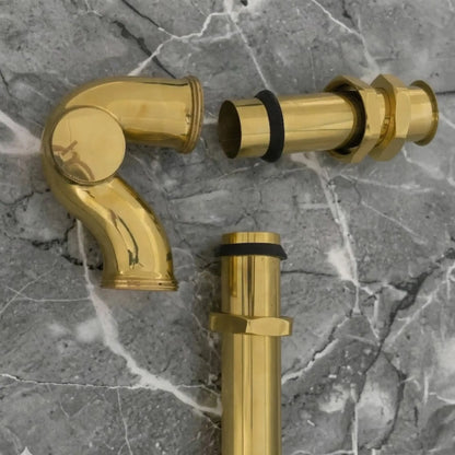 Solid unlacquered brass bathroom sink P-trap drain kit with exposed brass plumbing parts on gray marble surface