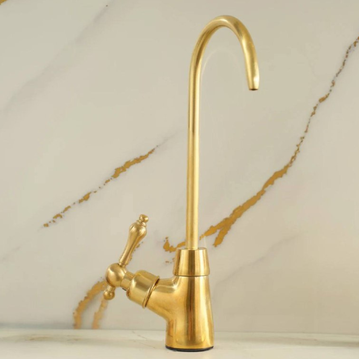 High-arc goose-neck beverage faucet in unlacquered brass against a marble backsplash